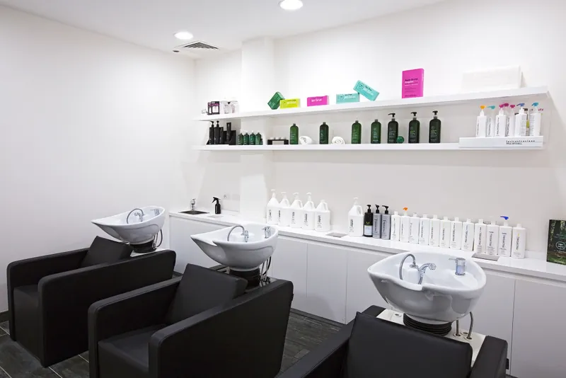 Tre postazioni lavaggio con poltrone nere e mensole di prodotti Paul Mitchell